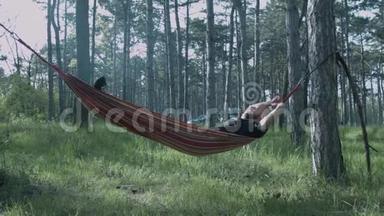 一个年轻人睡在森林里的吊床上。 游客正躺在吊床上。